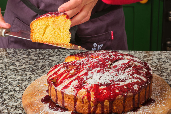 Woman holding a cake knife, serving a slice of cake from a wooden chopping board