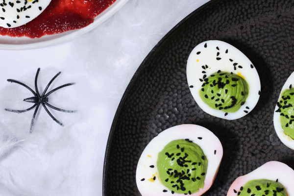 Green Deviled Eggs on a black plate with cobwebs and spiders